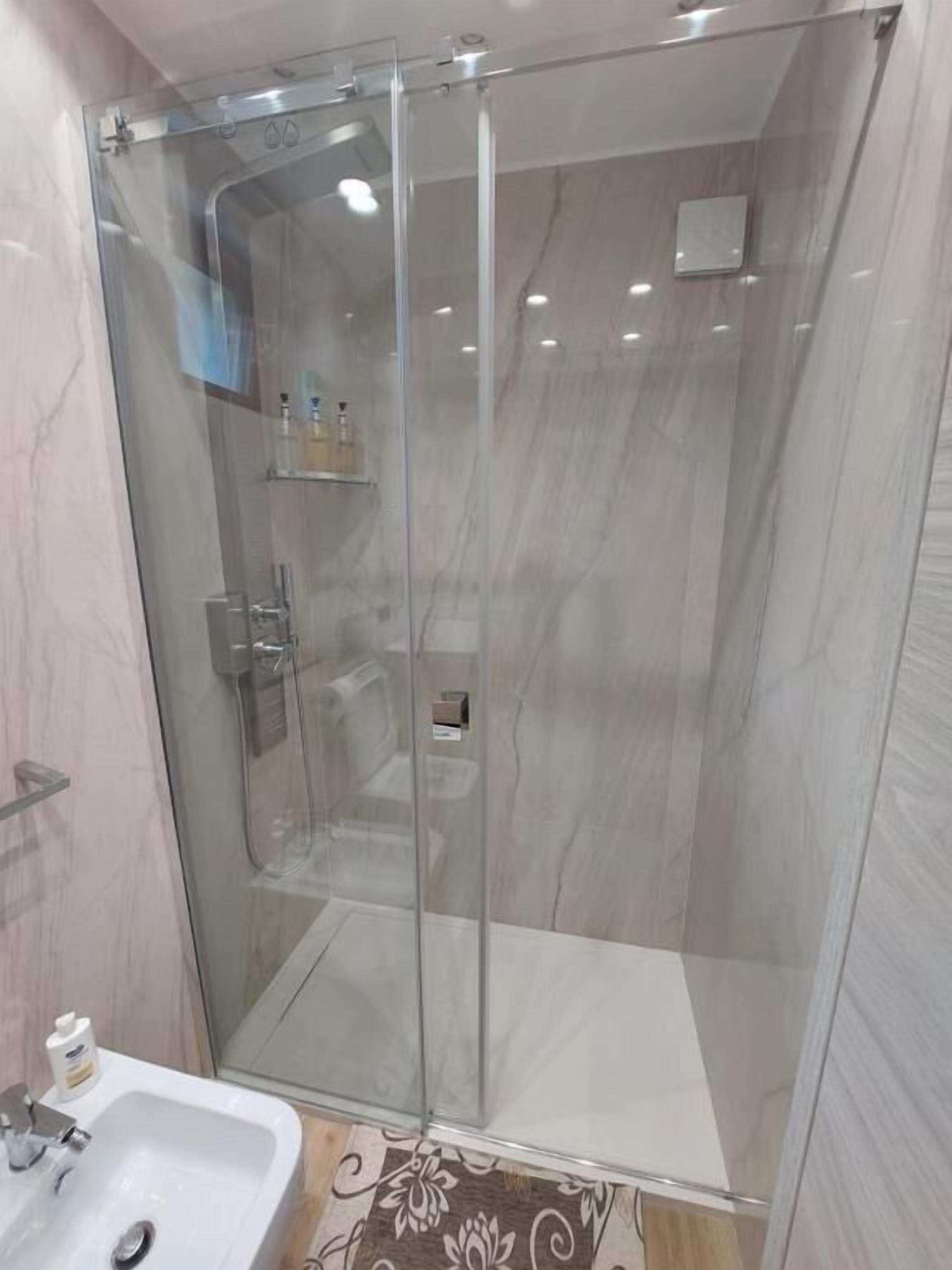 Un área de ducha con paredes de vidrio, un lavamanos blanco y un suelo con diseño de mármol.