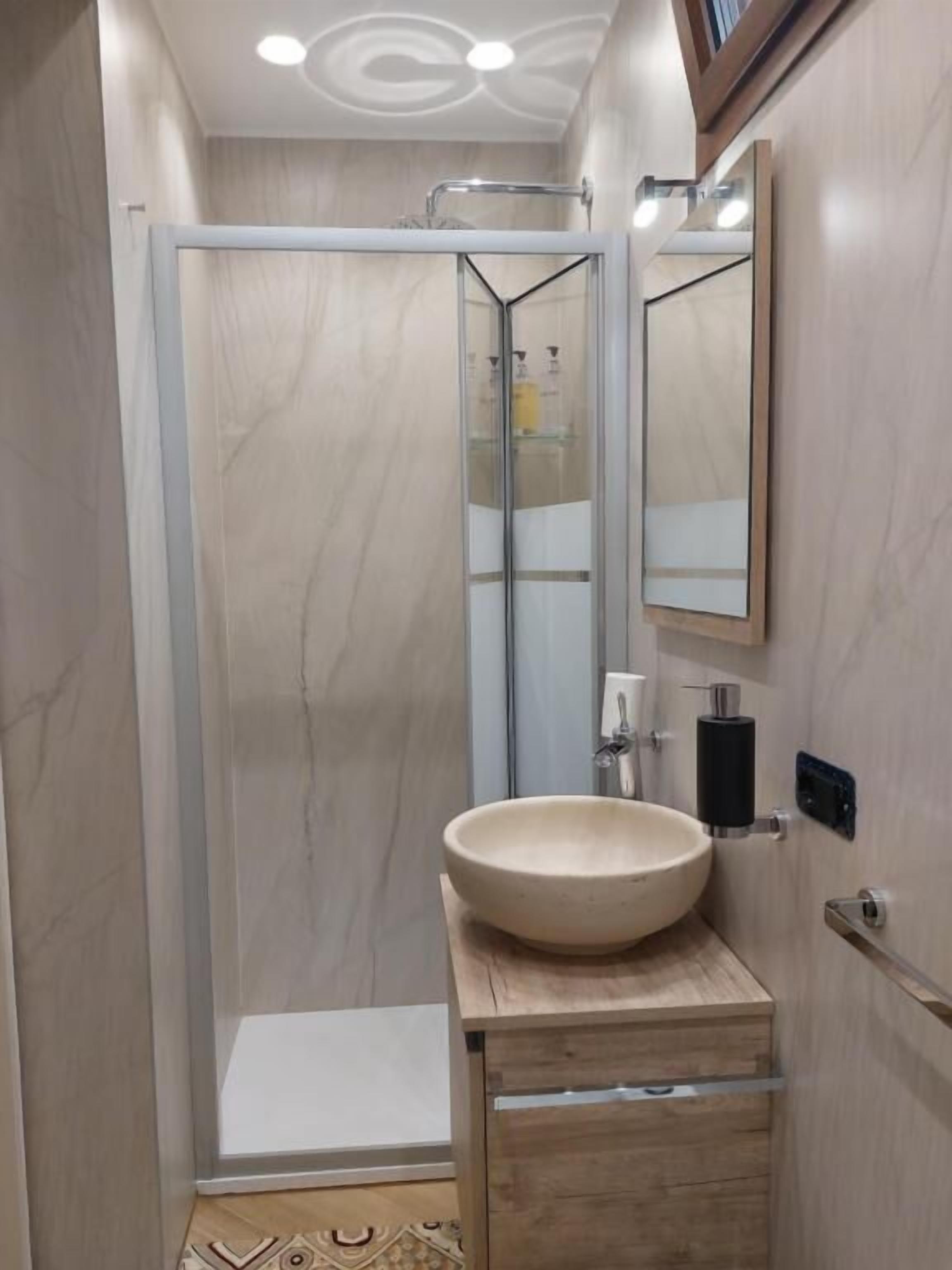 A bathroom with a glass shower enclosure, a wooden vanity with a bowl sink, and a mirror.