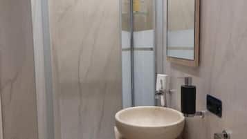 A bathroom with a glass shower enclosure, a wooden vanity with a bowl sink, and a mirror.