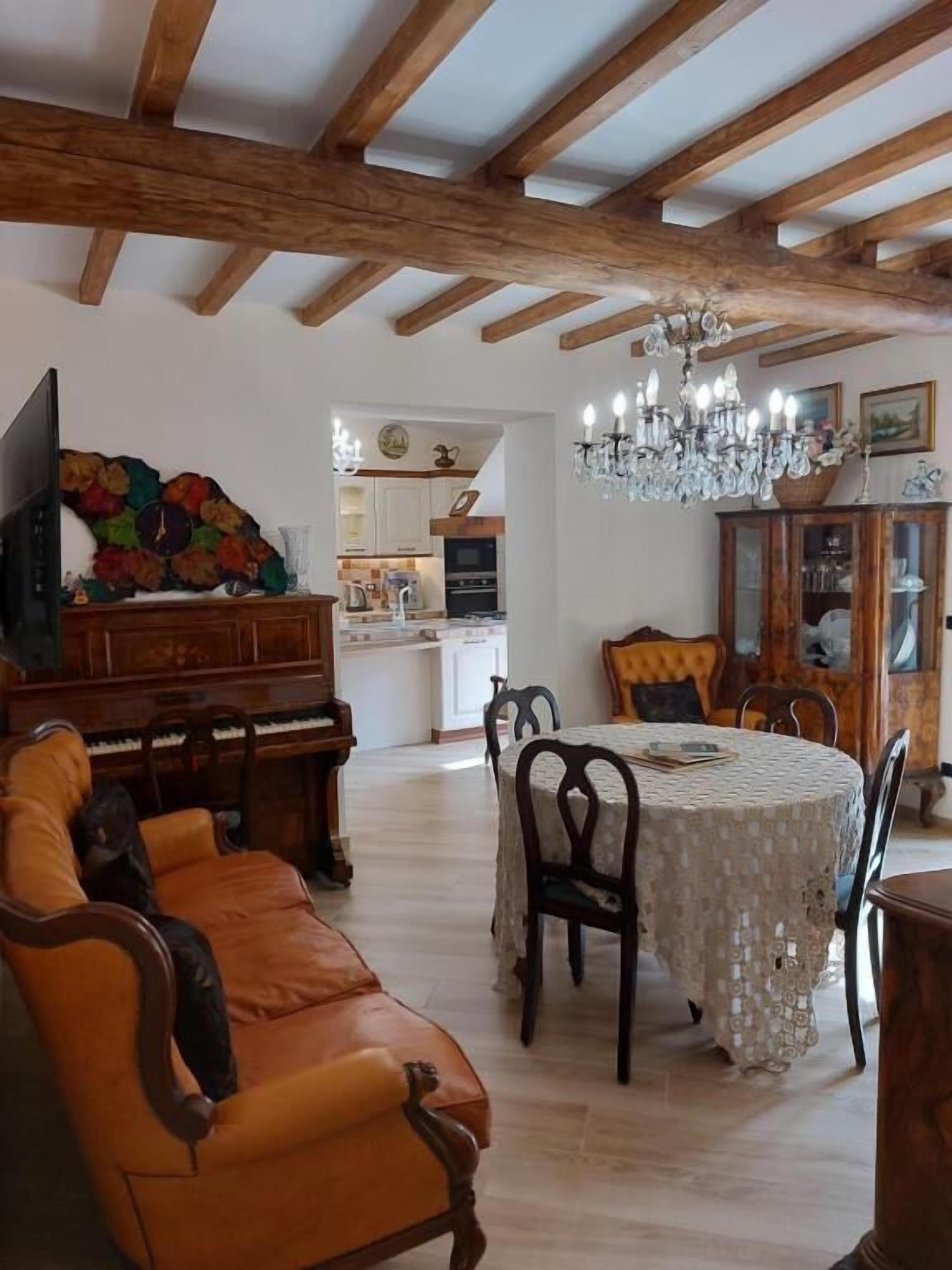 A dining area with a table set for four, wooden chairs, a chandelier, and a piano in the background.