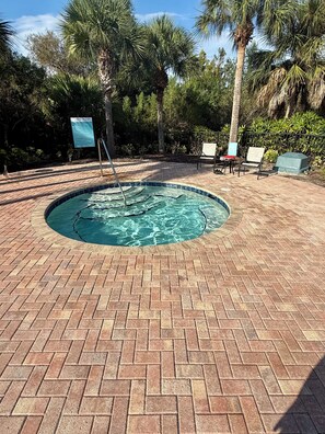A circular hot tub surrounded by a brick patio, with palm trees and a sign indicating spa rules. - Spacious 4-bedroom house with pool and gym access not far from beaches! (Palmetto)