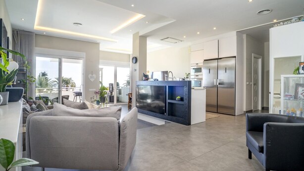 A modern living room with a sofa, a TV, and a kitchen area with a fridge and microwave. - Rg133 - Spacious 3 bed Apartment in Prime Location (Marbella)
