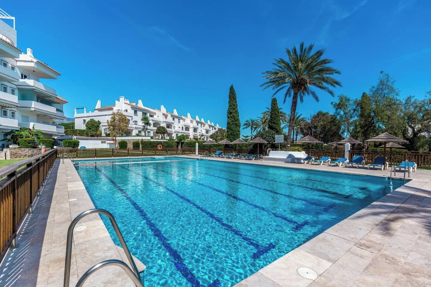Une piscine à l’eau d’un bleu cristallin, entourée de chaises longues et de parasols, avec un bâtiment visible à l’arrière-plan.