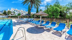 A pool area with lounge chairs and umbrellas, surrounded by palm trees and buildings. - Rg133 - Spacious 3 bed Apartment in Prime Location (Marbella)