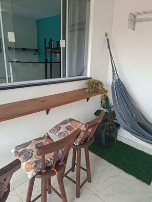 A balcony with a wooden bench, two chairs, a hammock, and a potted plant. - Fully furnished apartment, close to the beach and city center. (Armação dos Búzios)