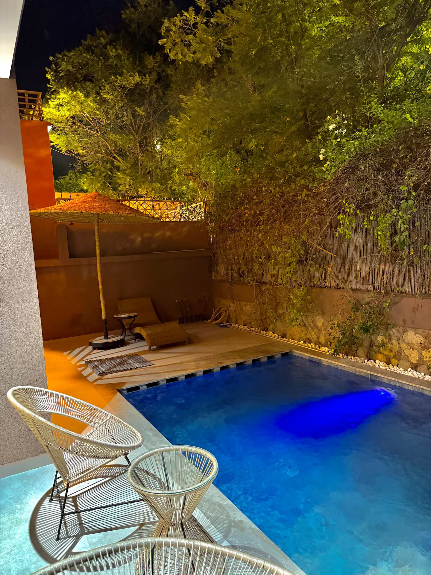 A swimming pool with a clear blue water surface, surrounded by a wooden deck and a bamboo fence.