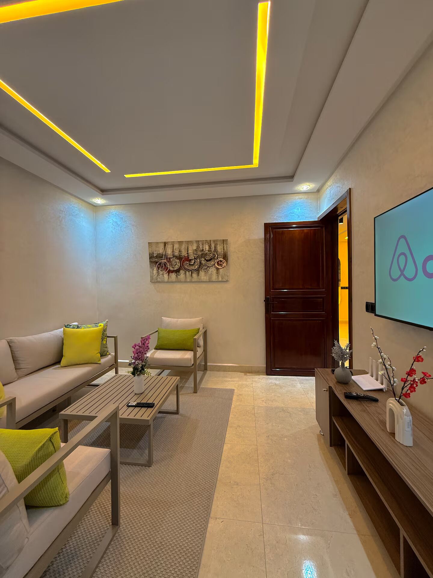 A modern living room with a sofa, armchair, coffee table, and a TV mounted on the wall.