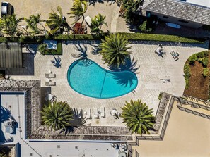 Luchtbeeld van een resort met een centraal zwembad, omgeven door palmbomen en ligbedden.