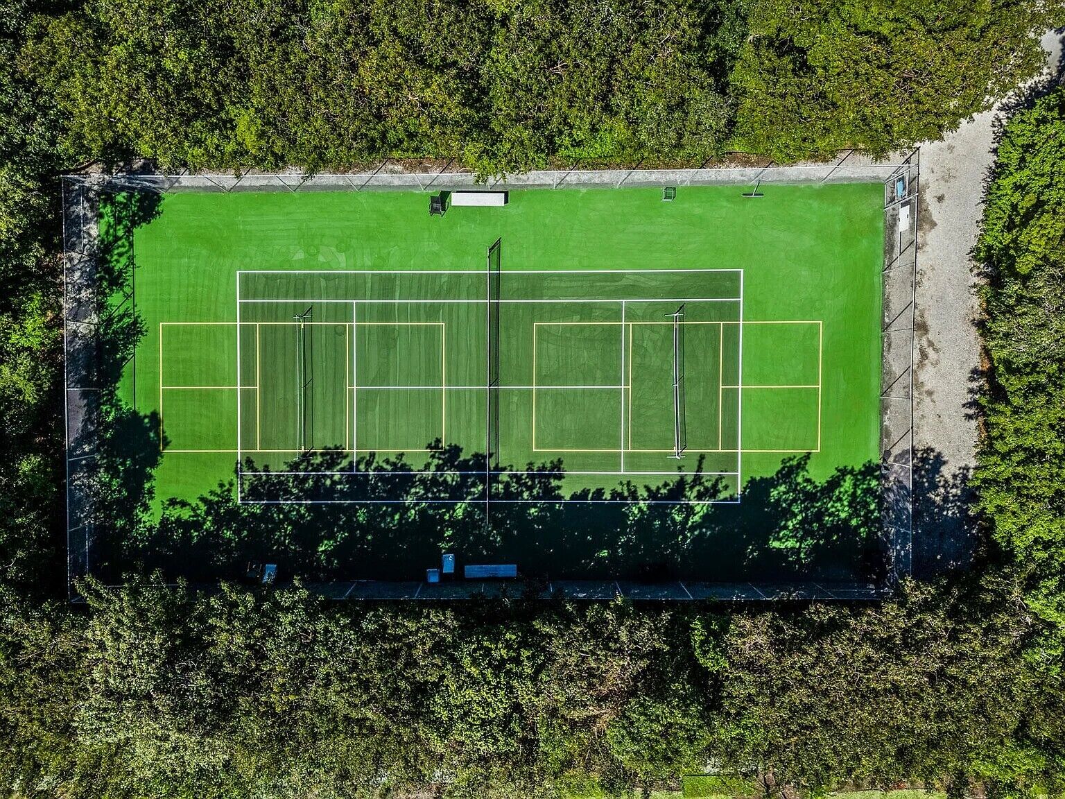 An aerial view of a sports field with multiple courts, surrounded by dense foliage.