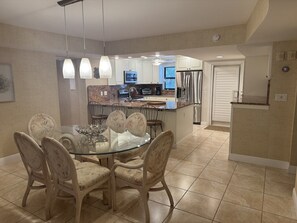 A dining area with a glass table and chairs, a kitchen in the background, and a door leading to another room. - Serene 3-bedroom condo in Buttonwood Bay, Key Largo perfect for relaxing getaway (Key Largo)