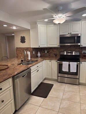 A modern kitchen with white cabinets, stainless steel appliances, a granite countertop, and a ceiling fan. - Serene 3-bedroom condo in Buttonwood Bay, Key Largo perfect for relaxing getaway (Key Largo)