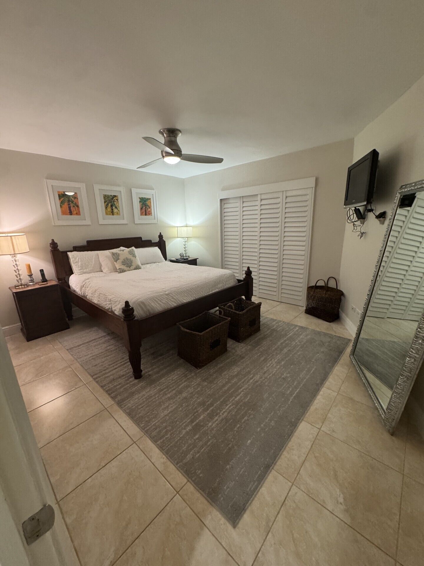 A bedroom with a bed, nightstands, a ceiling fan, a TV, a mirror, and a wardrobe.