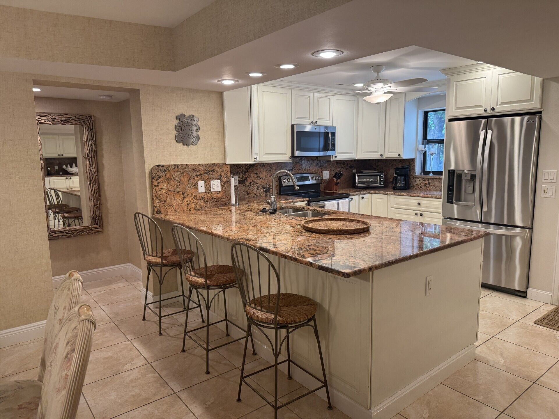 A modern kitchen with a central island, bar stools, stainless steel appliances, and a large mirror.