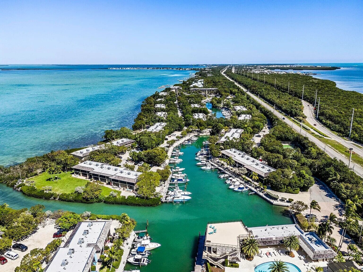 Vue aérienne d’une station balnéaire comprenant un port de plaisance, des villas pour les clients et une piscine.