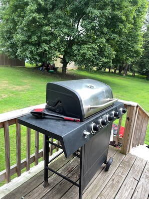 A barbecue grill on an outdoor deck with a wooden railing.