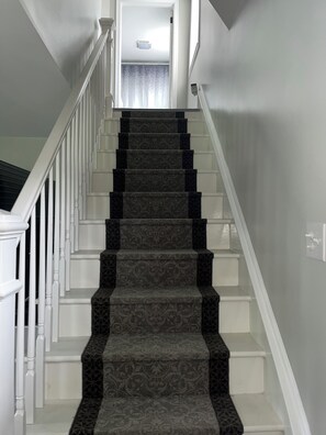 A staircase with a patterned carpet and white railings leading to a landing.