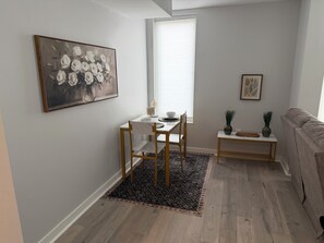 Ein modernes Wohnzimmer mit Essbereich, mit einem weißen Tisch, Holzstühlen, einem gemusterten Teppich und einem grauen Sofa.