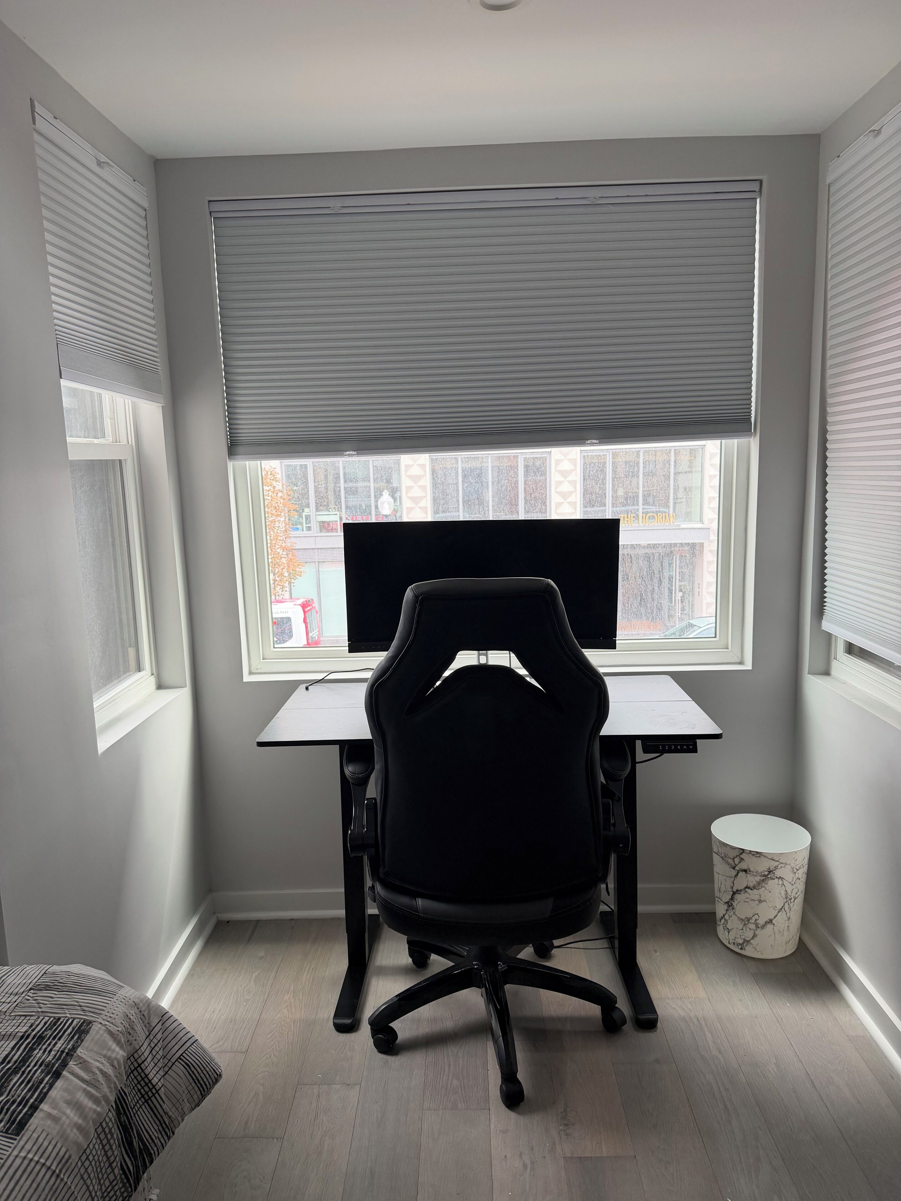 A room with a desk, a black office chair, a computer, and a window with blinds.
