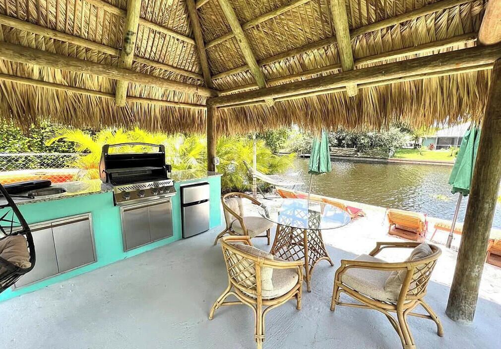 Une terrasse extérieure équipée d’un barbecue, de sièges et offrant une vue sur un plan d’eau.