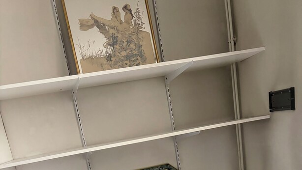 Um quarto com uma escrivaninha preta, uma cadeira branca, um quadro na parede e um radiador.