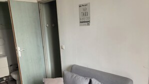 Quarto com um sofá cinzento, uma pequena mesa redonda de madeira e uma porta que dá para um banheiro.