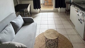 Um espaço compacto para viver, com sofá, mesa de centro redonda, mesa de jantar e cozinha compacta.
