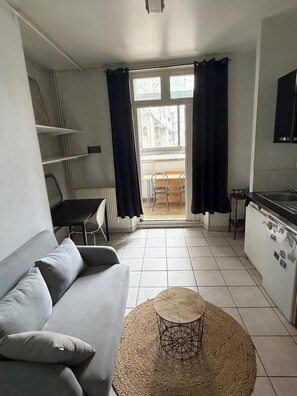 Ein kompakter Wohnraum mit Sofa, rundem Couchtisch, Esstisch und Küchenzeile.