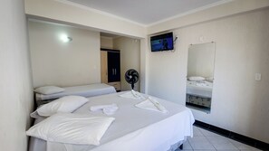 A hotel room with two beds, a TV mounted on the wall, a fan, and a mirror.