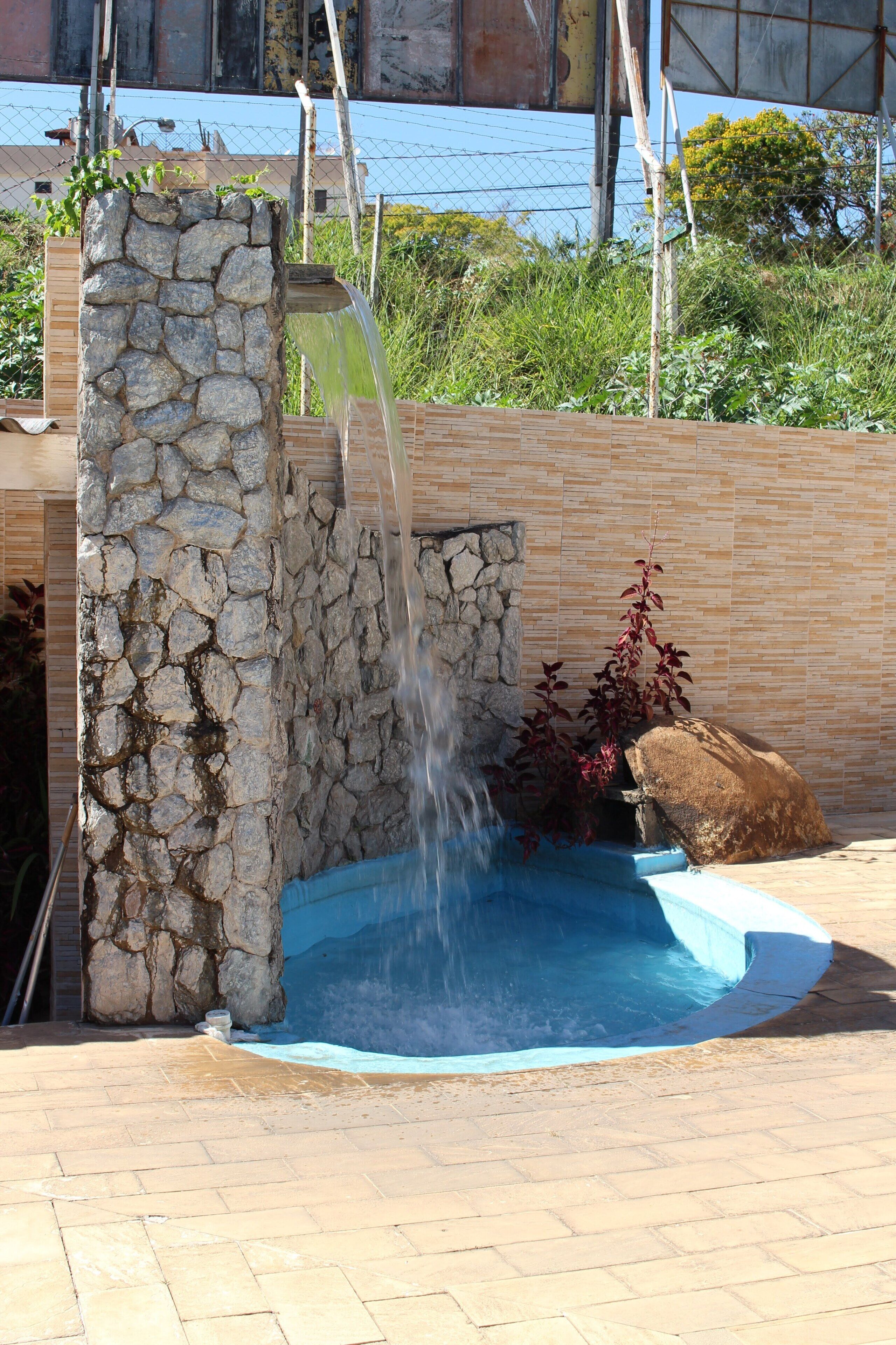 Une fontaine en pierre avec une cascade, un petit bassin et une clôture en bois en arrière-plan.