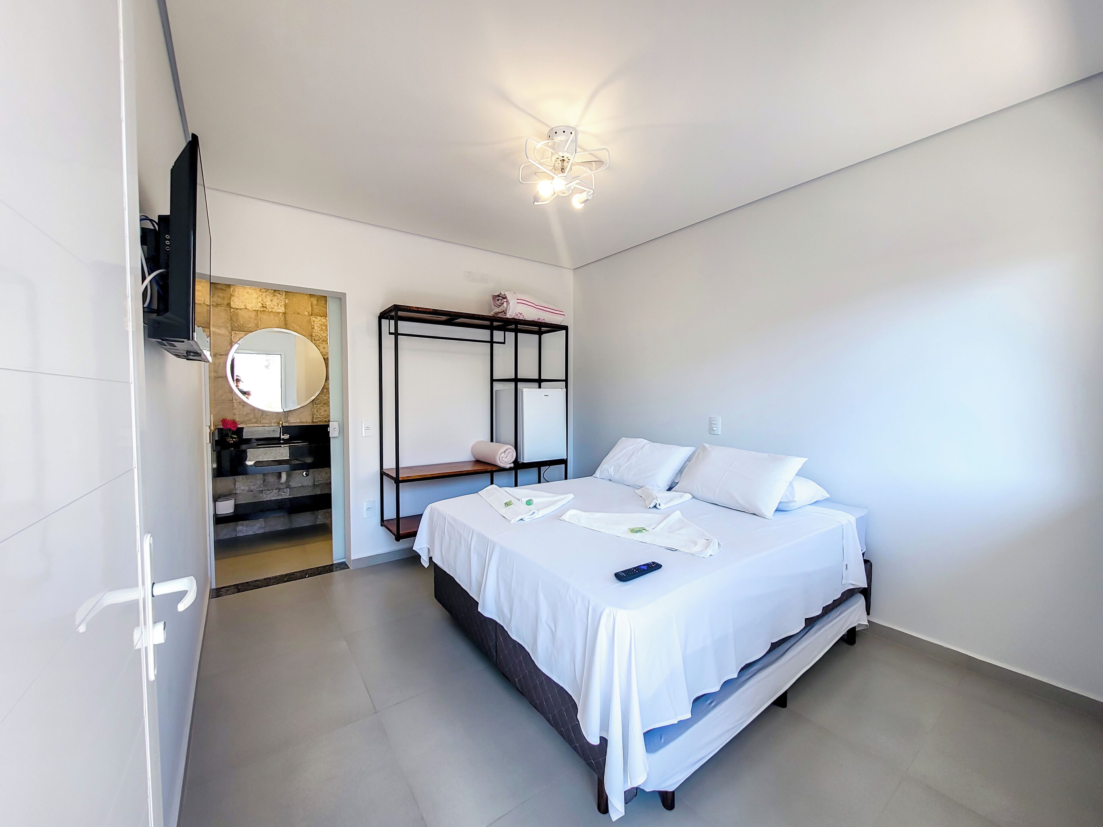 A modern hotel room with a bed, a built-in TV, a ceiling fan, and a bathroom visible through an open door.