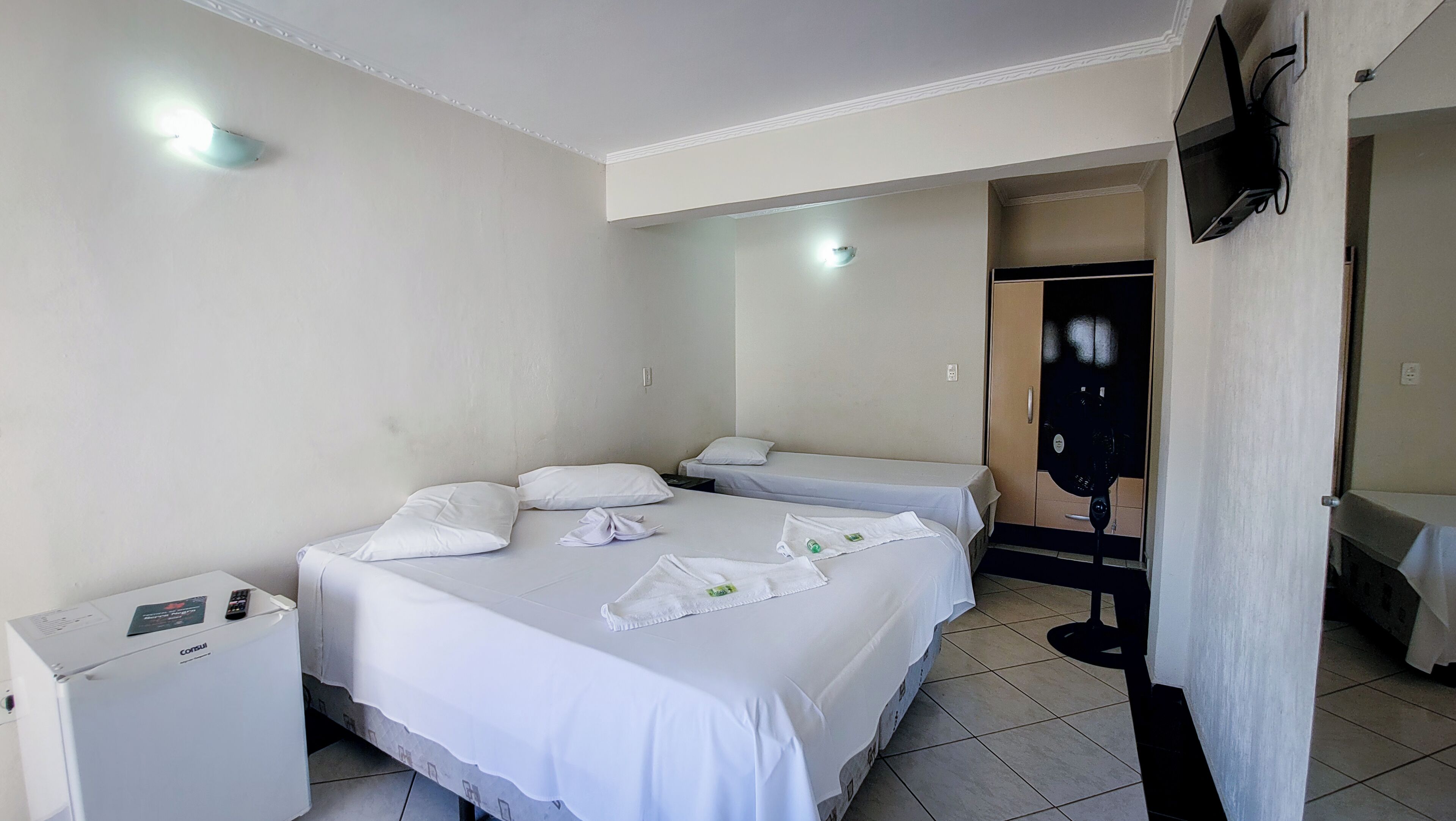 A hotel room with two beds, a minibar, a TV mounted on the wall, and a door leading to another room.
