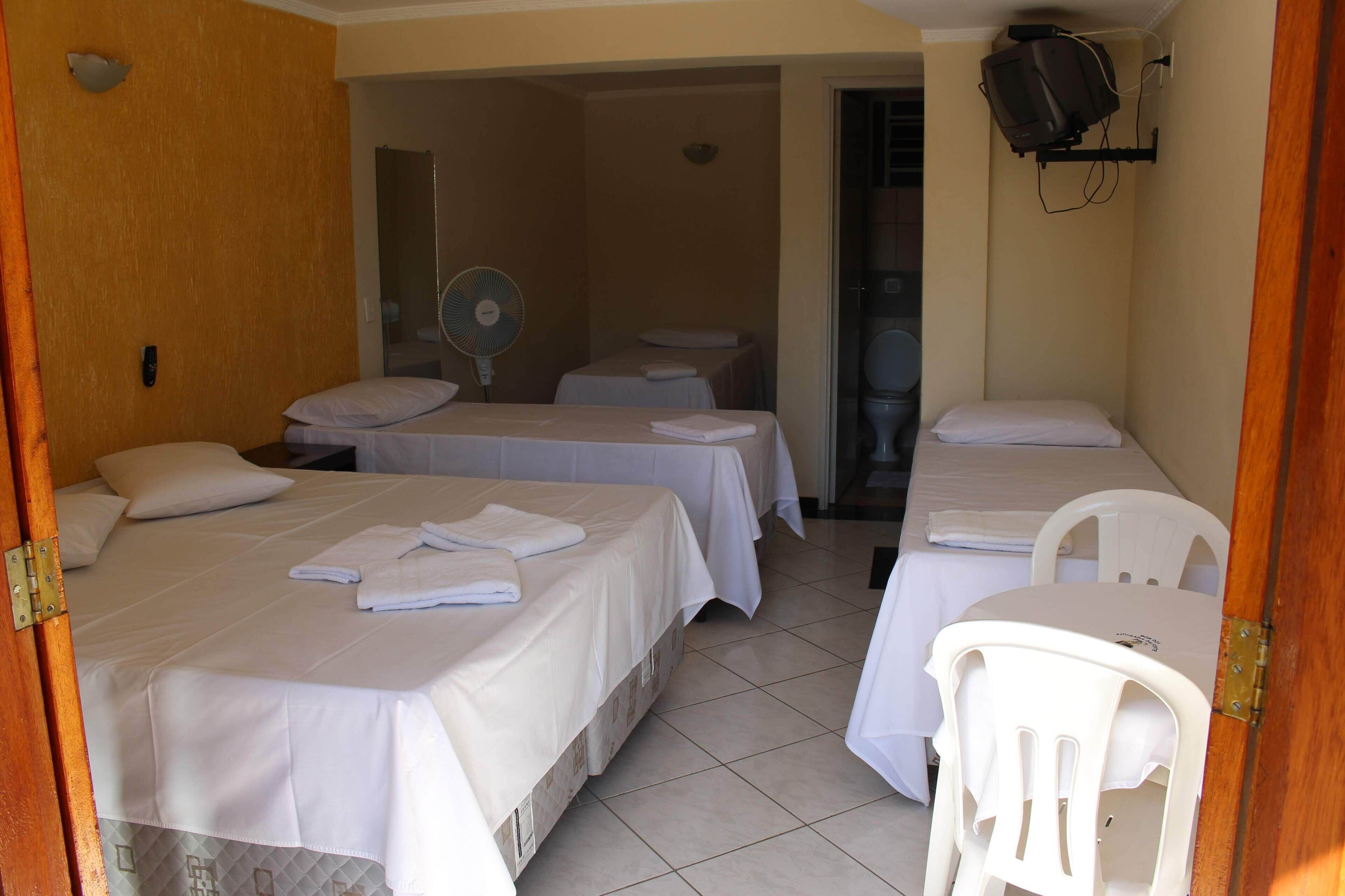 A hotel room with two beds, a fan, a TV, and a small table.