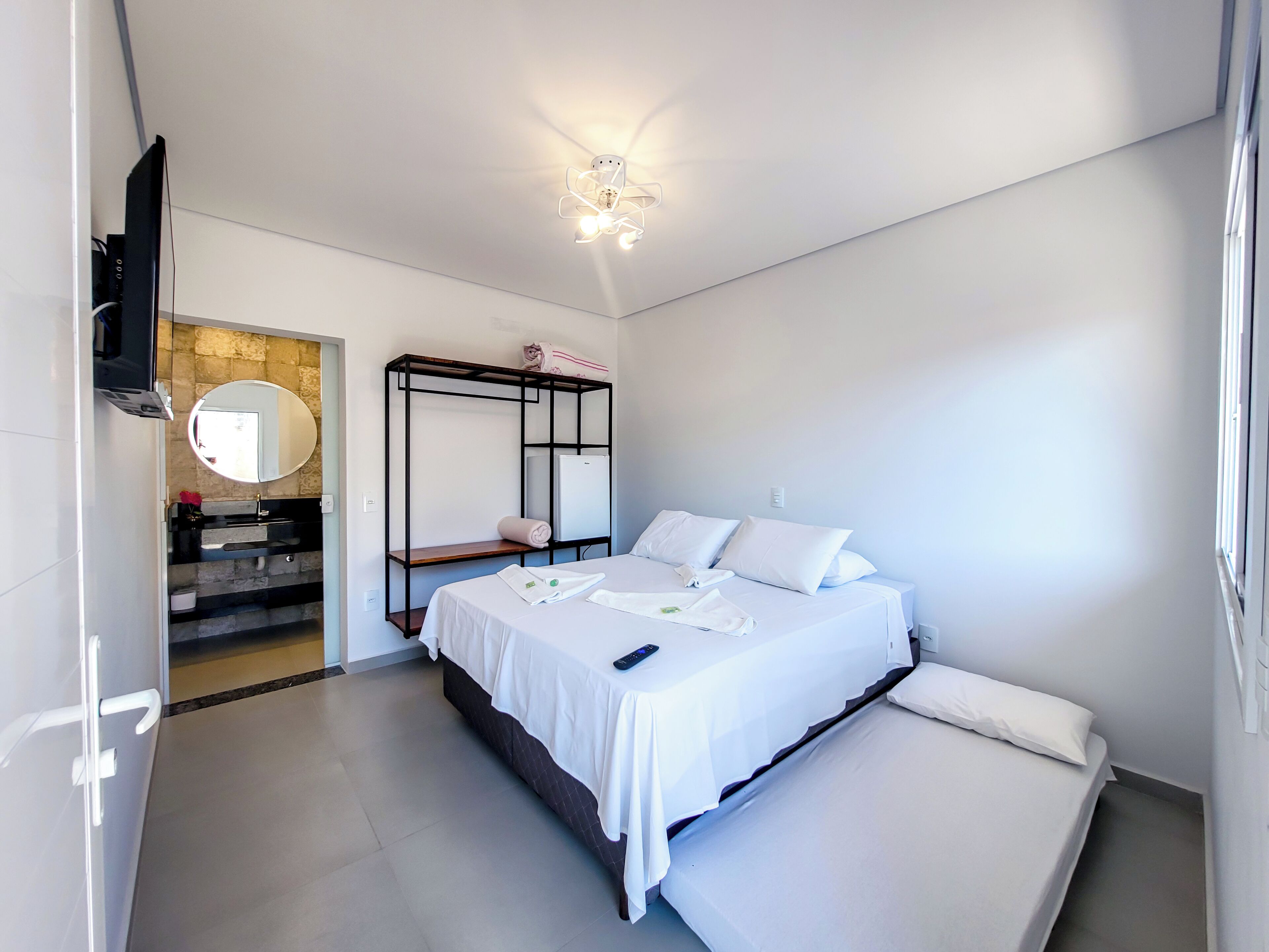 A modern hotel room with a bed, a built-in wardrobe, a mirror, and a ceiling light fixture.