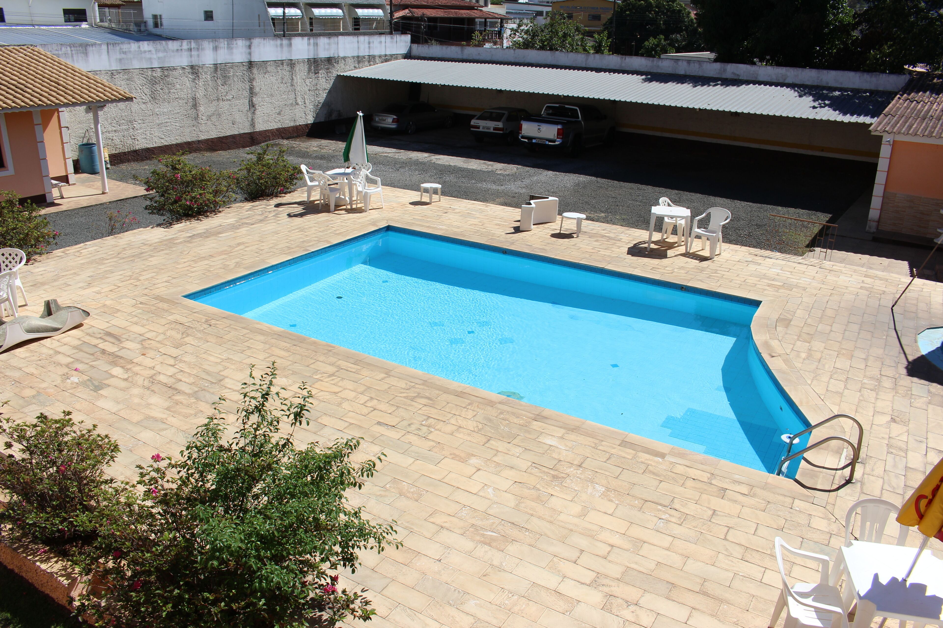 Una piscina rectangular con solárium empedrado, rodeada de sillas y mesas de plástico blanco.