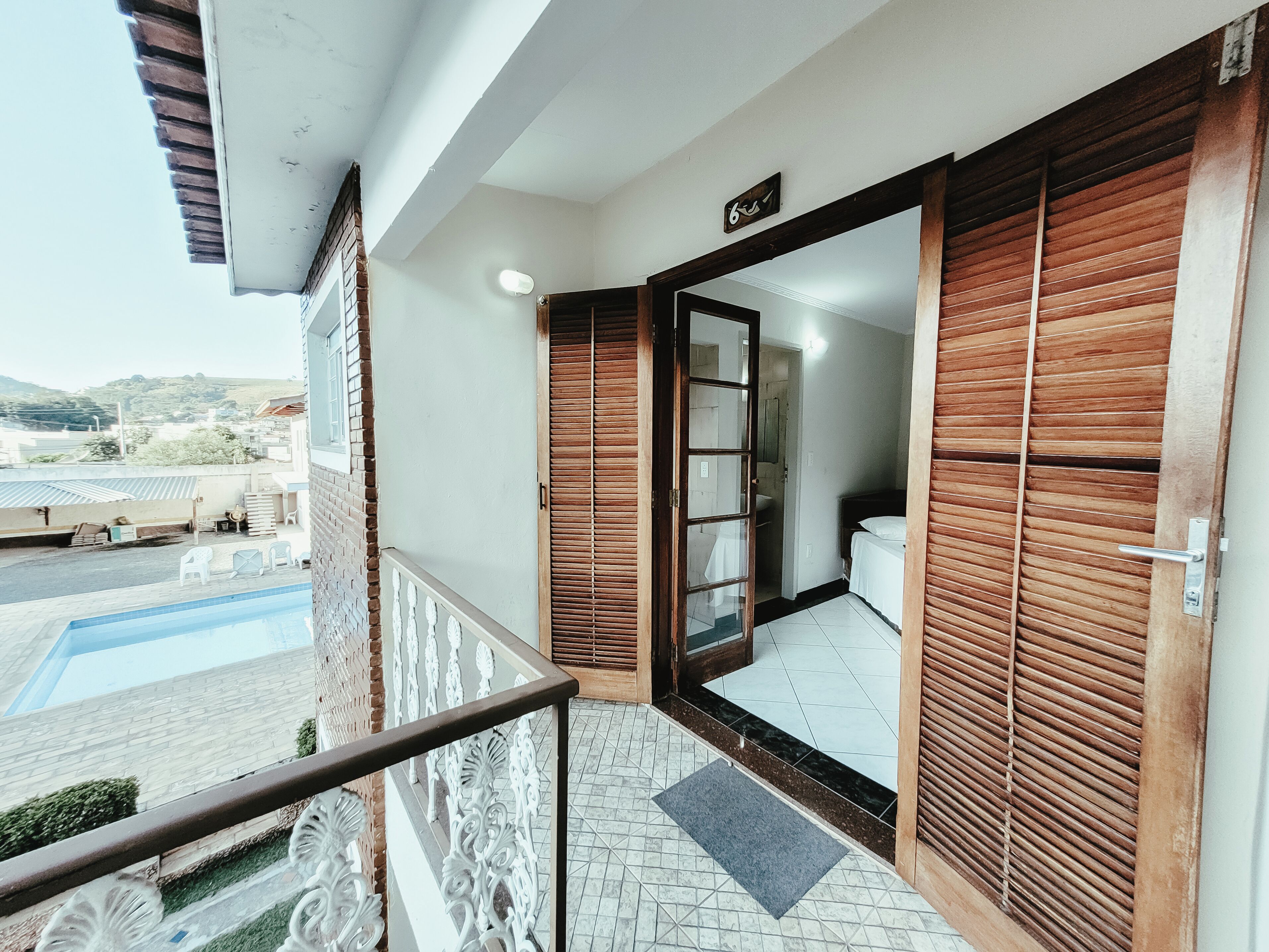Uma varanda com guarda-corpo de metal, uma piscina e vista para um edifício com telhado em azulejos.