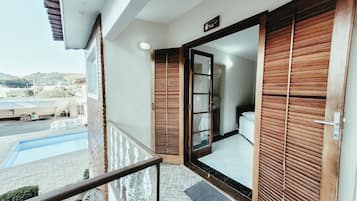 Uma varanda com guarda-corpo de metal, uma piscina e vista para um edifício com telhado em azulejos.