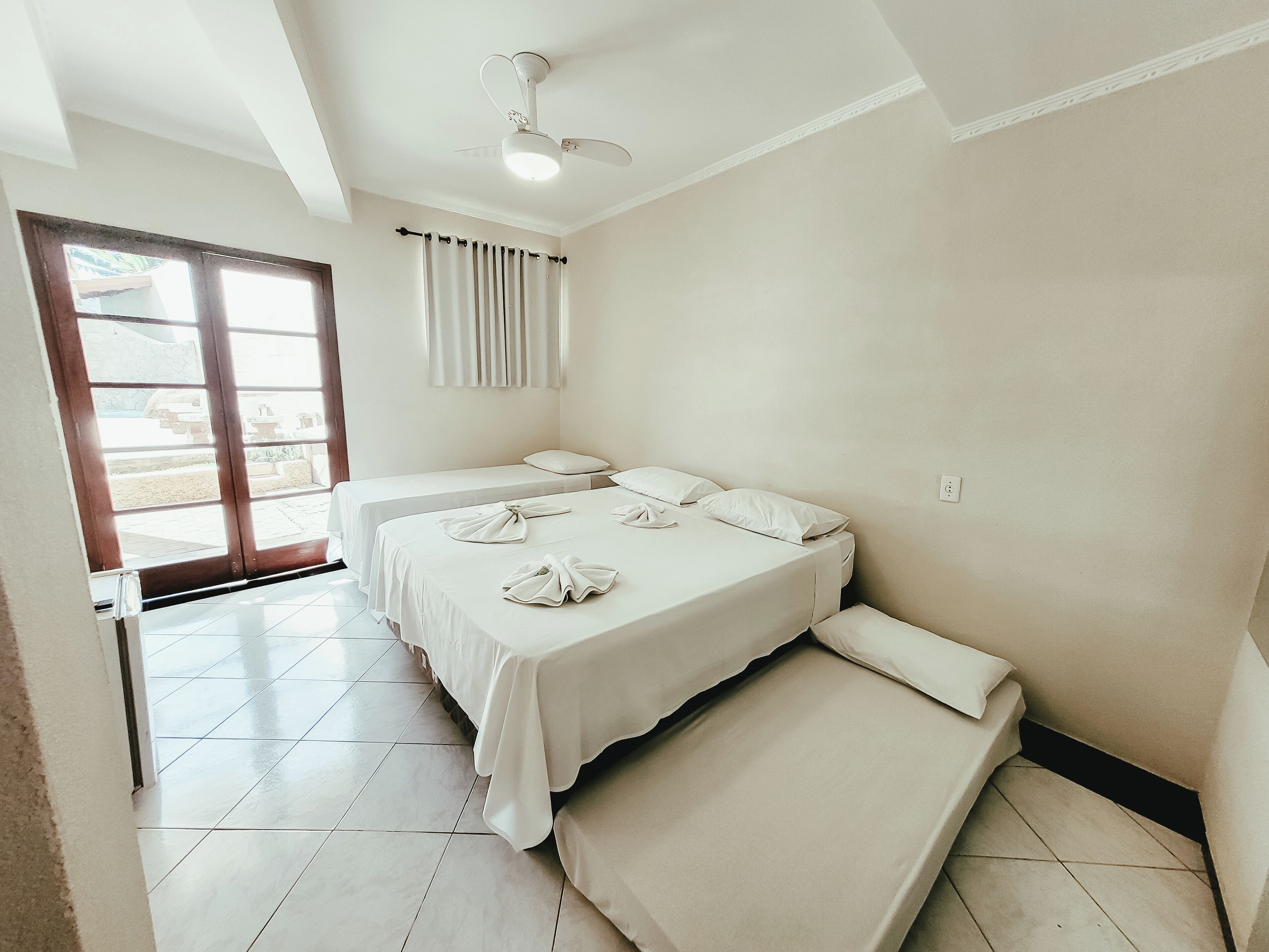 Quarto de hotel com duas camas, um ventilador de teto e vista através de uma porta de vidro.