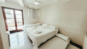 Quarto de hotel com duas camas, um ventilador de teto e vista através de uma porta de vidro.