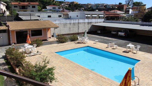 Una piscina con solárium alicatado, rodeada de mobiliario exterior y un pequeño edificio con techo rojo.