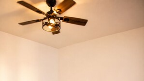 Una camera d'albergo con un letto, cuscini, una ventola a soffitto e un comodino con una lampada.