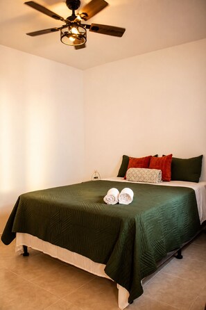 A hotel room with a bed, pillows, a ceiling fan, and a nightstand with a lamp. - Volcano Views Near Antigua! 3BR Retreat w/ Main-Floor Bedrooms (ciudad vieja)