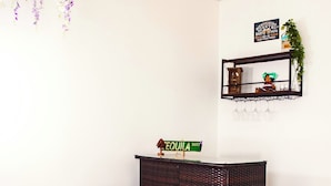Una stanza con un'area bar, due sgabelli da bar, un cartello con scritto 'TEQUILA WAY' e fiori viola appesi.