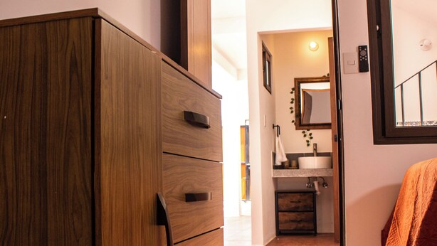 Un corridoio con un settimino di legno, uno specchio e un bagno con lavandino e asciugamano.