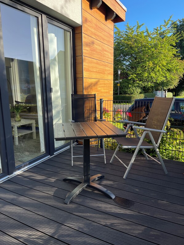 A deck with a table and chairs, a glass door, and a wooden wall.