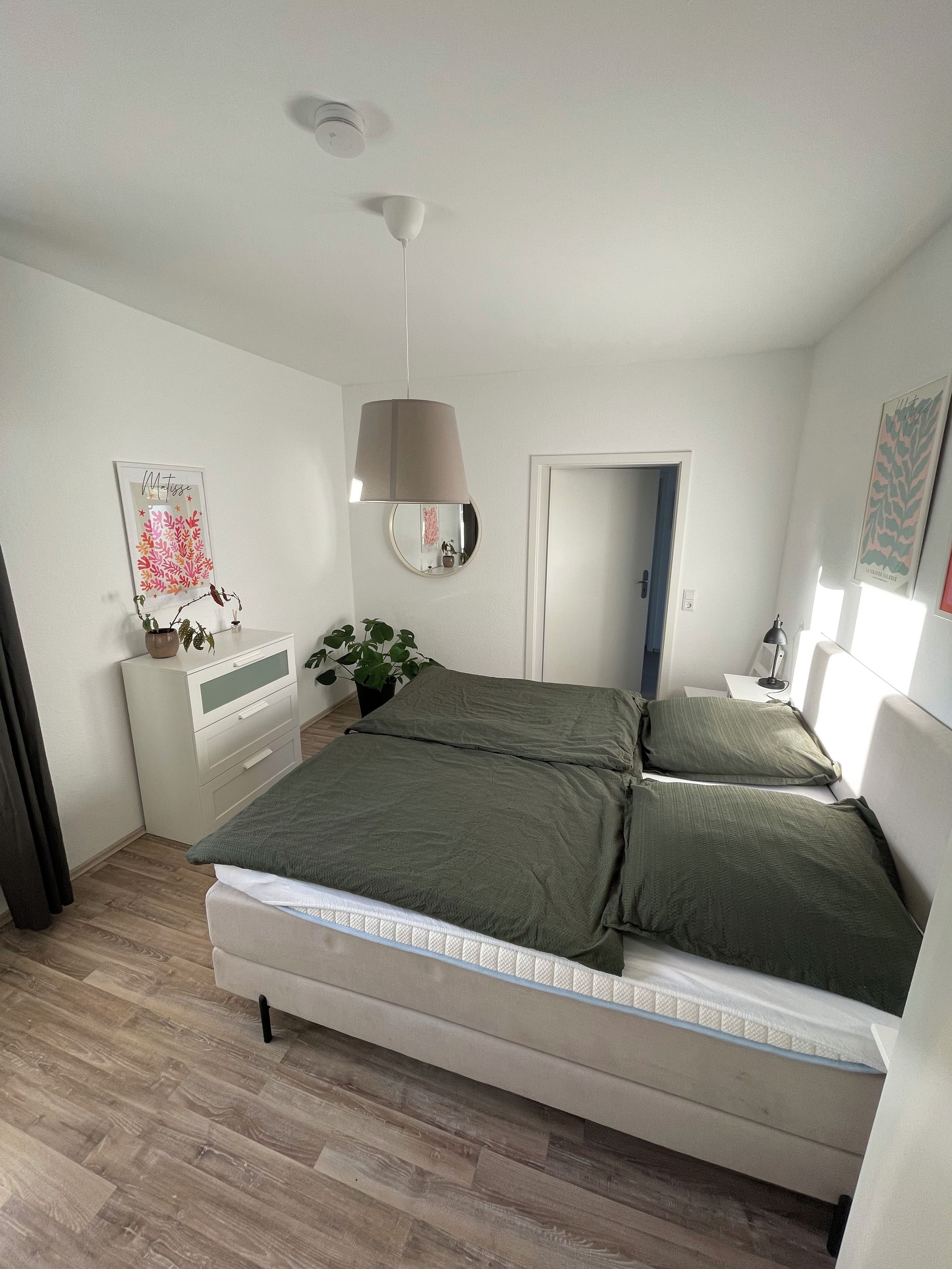 Ein Schlafzimmer mit Bett, Nachttischen, einem Spiegel und einer Tür.