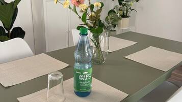 A dining table with a water bottle, a vase with flowers, and a framed picture on the wall.