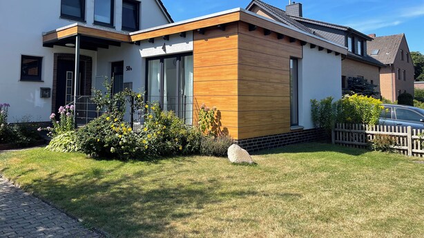 A modern two-story house with a white facade, large windows, and a wooden extension.