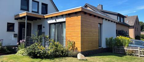 Une maison moderne à deux étages, dotée d’une façade blanche, de grandes fenêtres et d’une extension en bois.