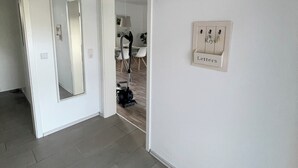 A hallway with a vacuum cleaner, a mirror, and a wall-mounted light switch.