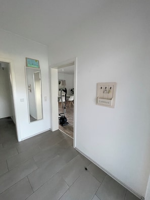 A hallway with a vacuum cleaner, a mirror, and a wall-mounted light switch.